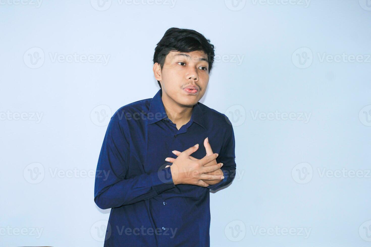 jovem ásia homem é relaxante a partir de coração ataque dor fazendo inalar e exalando face expressão e gesto vestindo marinha camisa foto