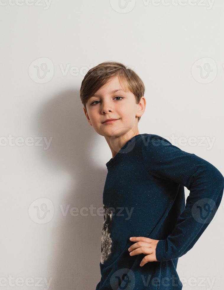 um lindo garoto parado perto de uma parede branca, sorrindo foto