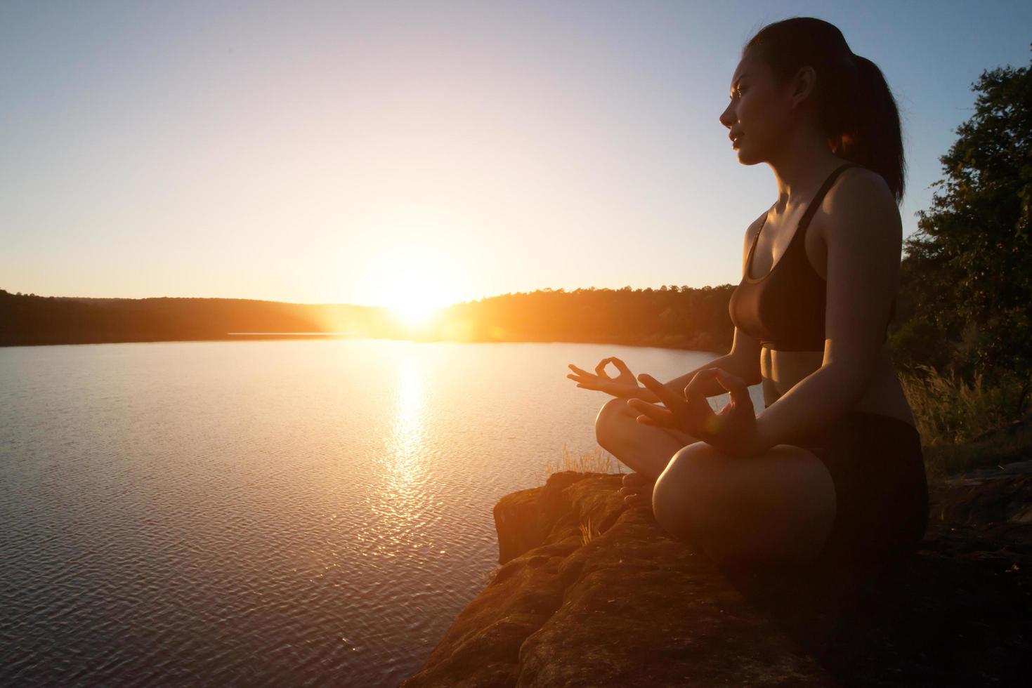 jovem mulher saudável está praticando ioga no lago da montanha durante o pôr do sol. foto