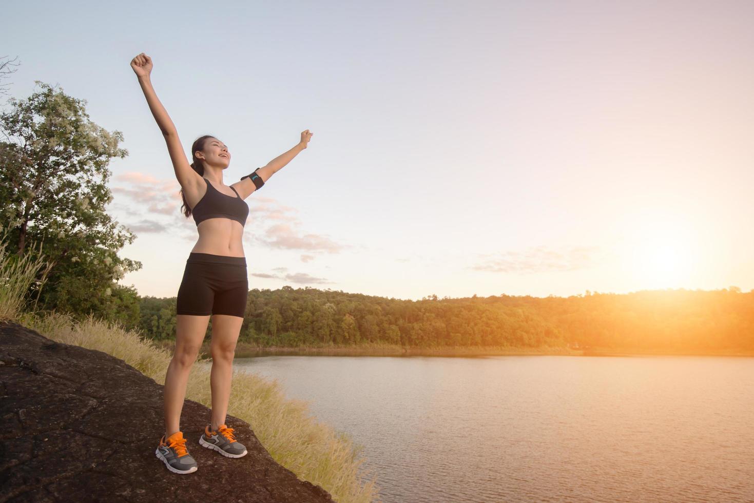 jovem fitness mulher alcançar caminhadas no pico com vista para o lago do pôr do sol. foto