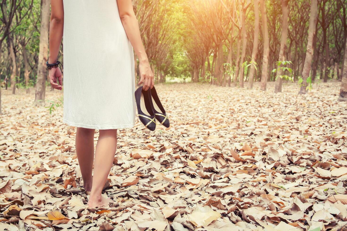 costas de uma jovem carregando sapatos e caminhando na floresta verde foto