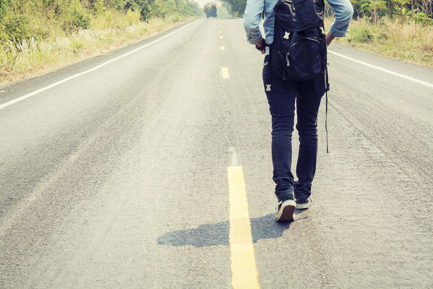 jovem pedindo carona carregando uma mochila sentada na estrada foto