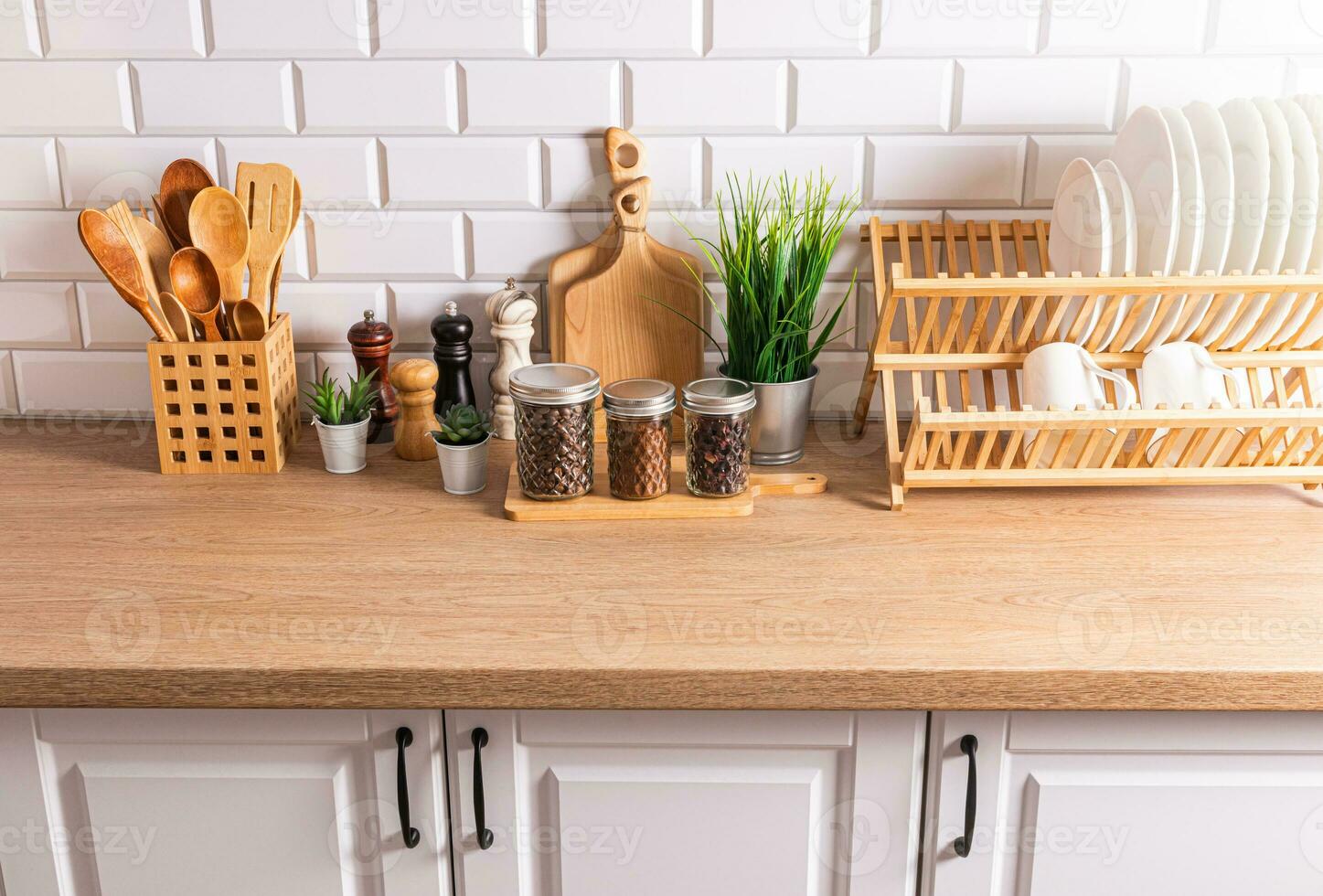 uma conjunto do à moda cozinha utensílios pratos, tigelas, corte Pranchas, colheres em uma de madeira bancada oposto uma branco tijolo muro. foto