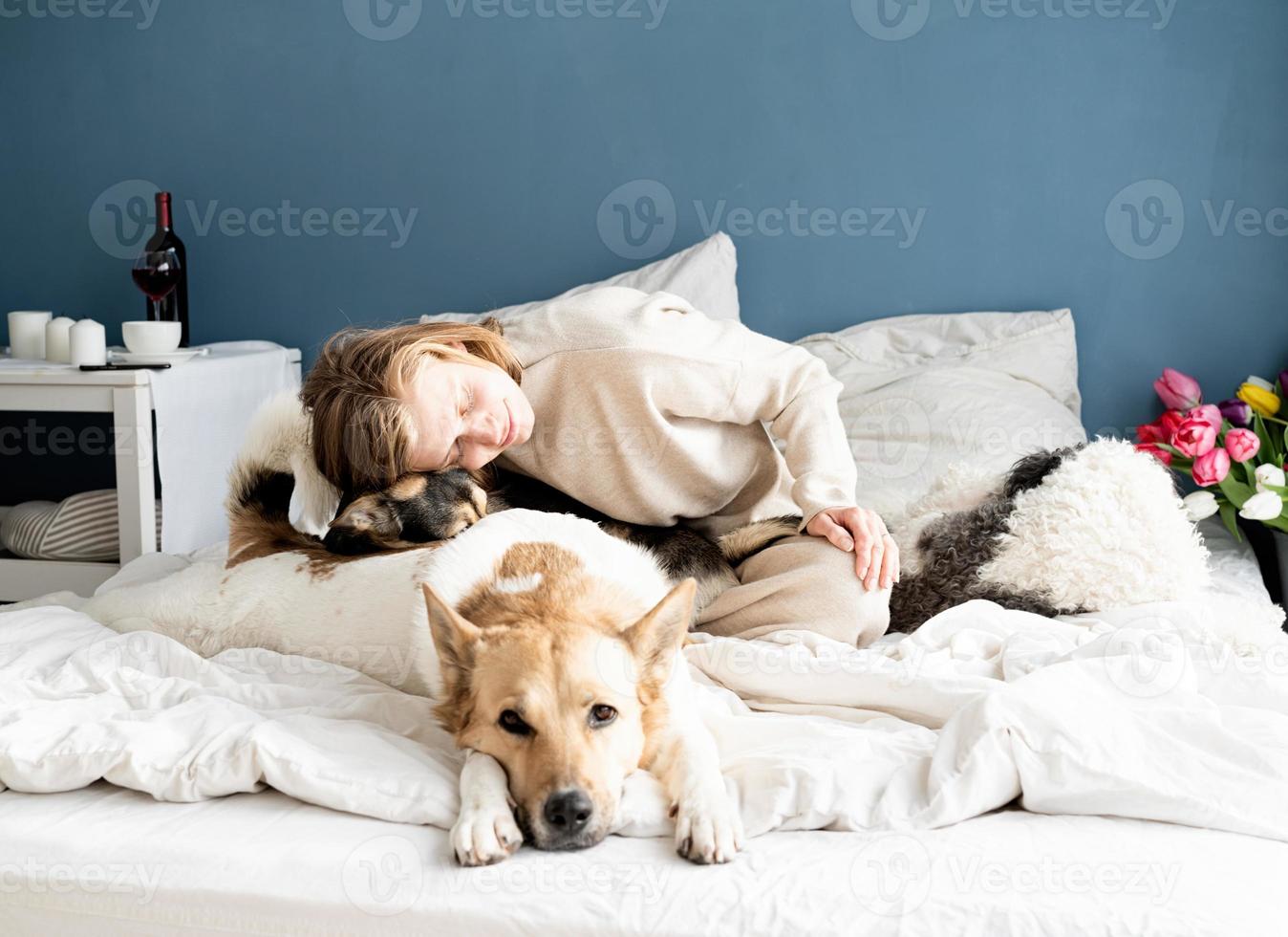 jovem feliz sentada na cama brincando com seus cachorros foto