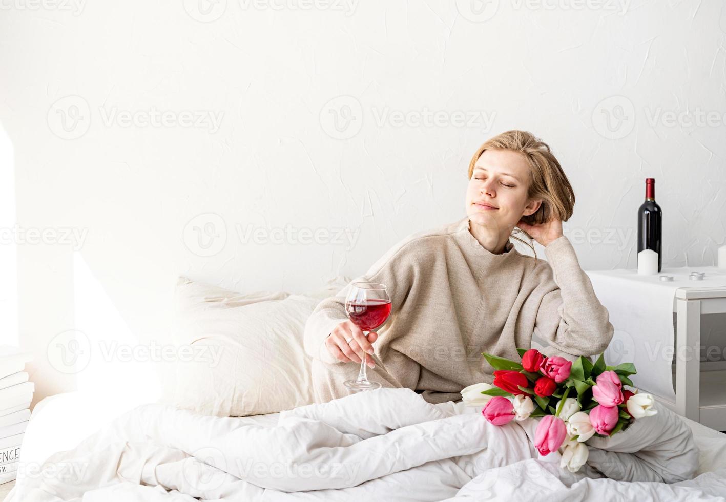 mulher sentada na cama de pijama segurando uma taça de vinho foto