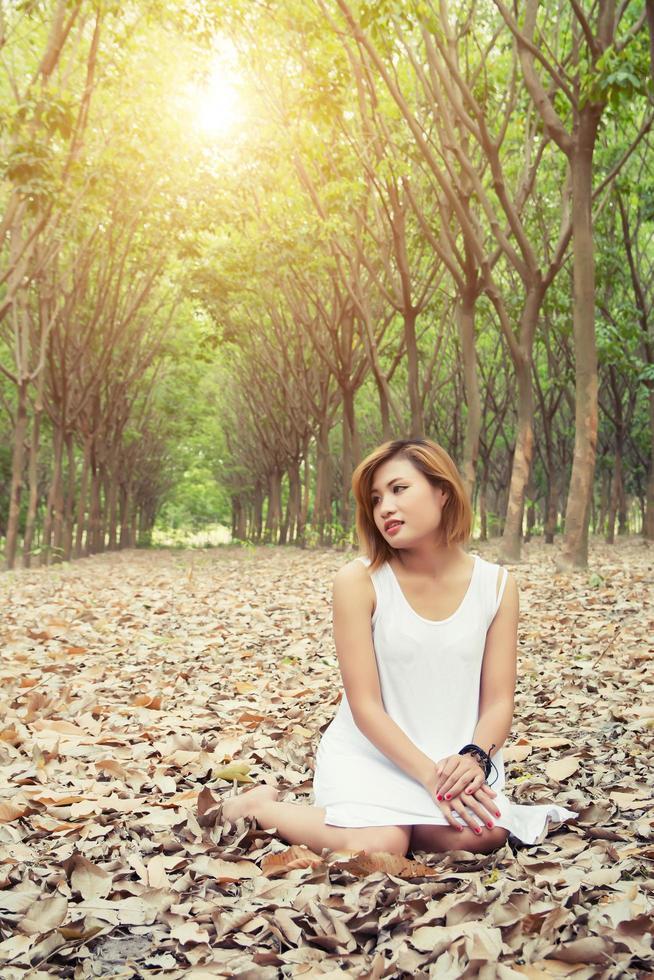 bela jovem asiática sentada nas folhas secas na floresta foto