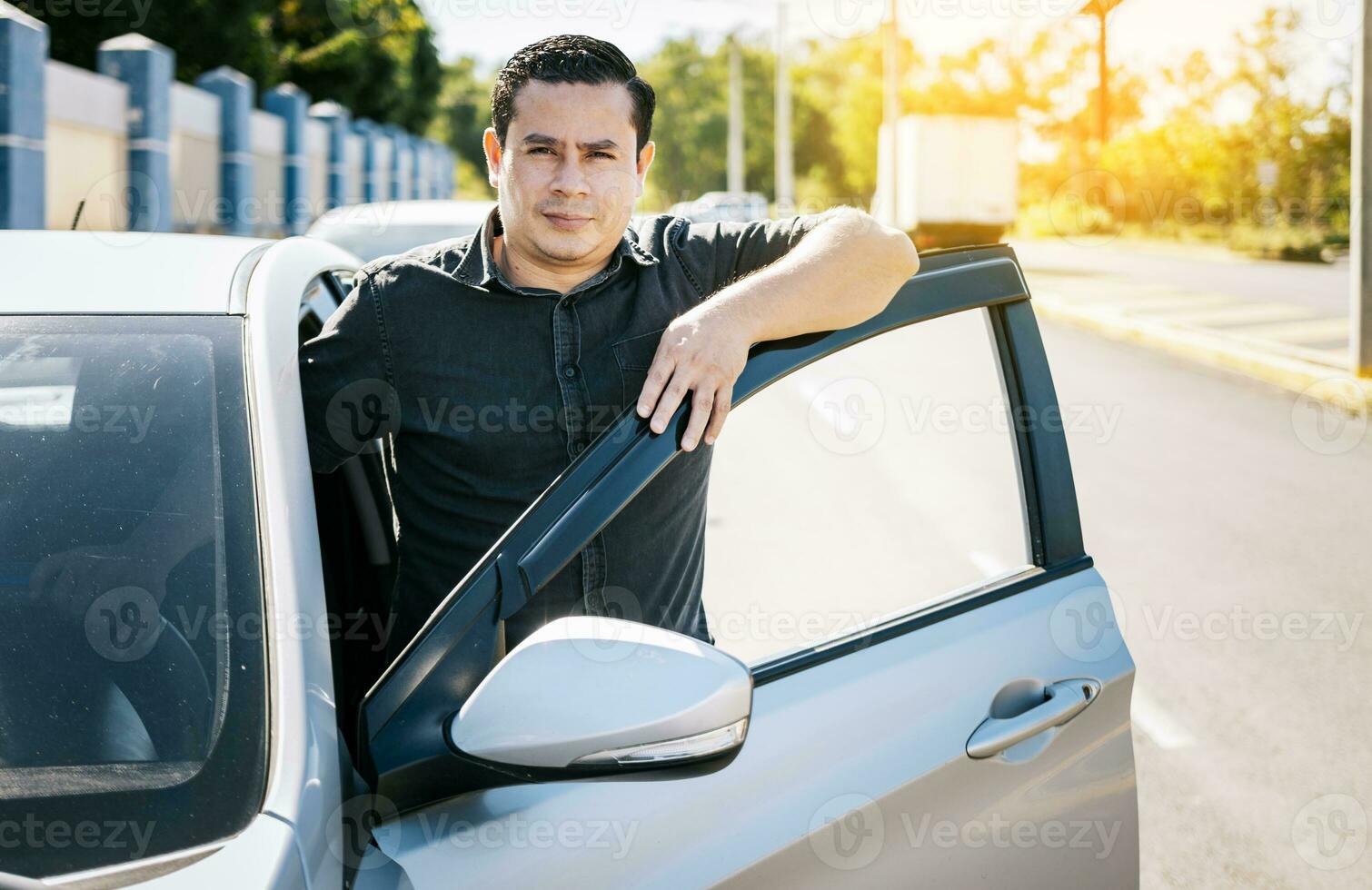 fechar acima do motorista inclinado em a carro porta dentro a rua, jovem latim homem inclinado em carro porta dentro a rua. sorridente motorista inclinado em a carro porta. sorridente proprietário com Novo carro foto