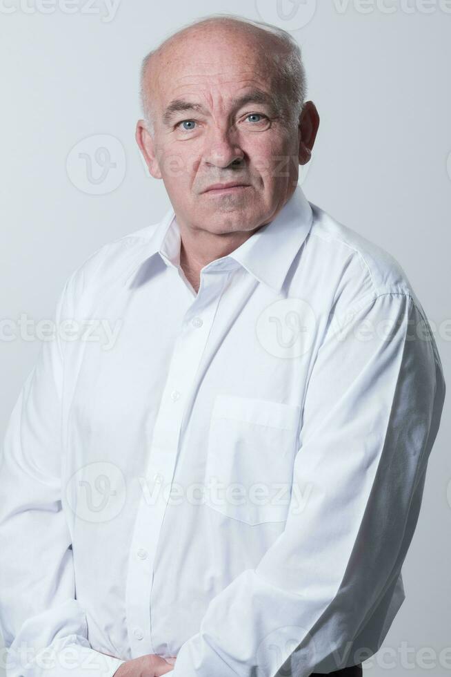 retrato do a Mais velho homem vestindo uma branco camisa em uma cinzento fundo. uma saudável velho homem parece às uma Câmera isolado sobre uma cinzento muro. a Mais velho homem sorrisos às a Câmera, uma feliz velho cara. foto