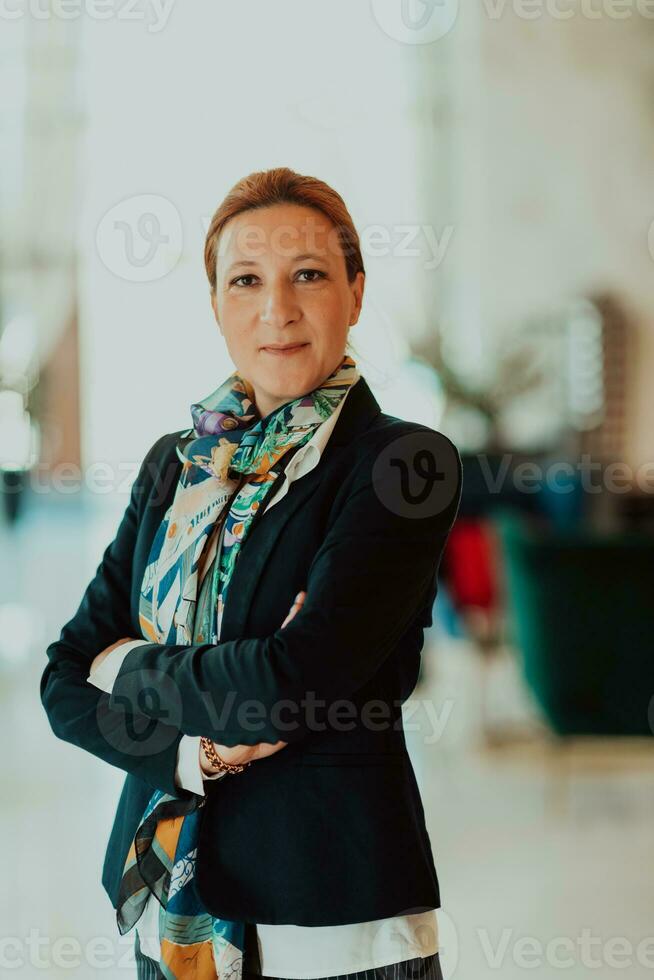 retrato do o negócio Senior mulher com cruzado braços em pé dentro moderno corporação. seletivo foco foto