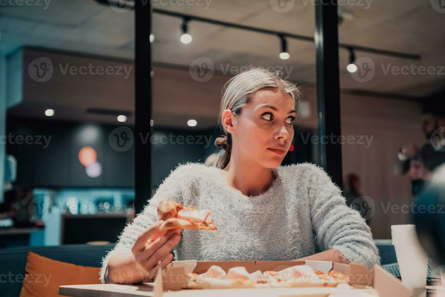 uma moderno Loiras comendo pizza dentro dela escritório em uma pausa a partir de trabalhos foto