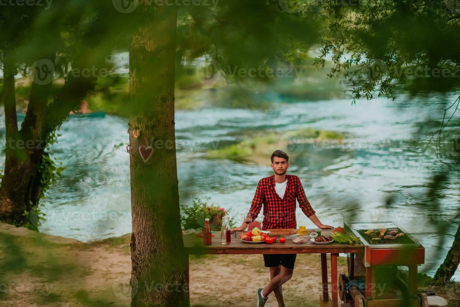 uma homem preparando uma delicioso jantar para dele amigos quem estão tendo Diversão de a rio dentro natureza foto