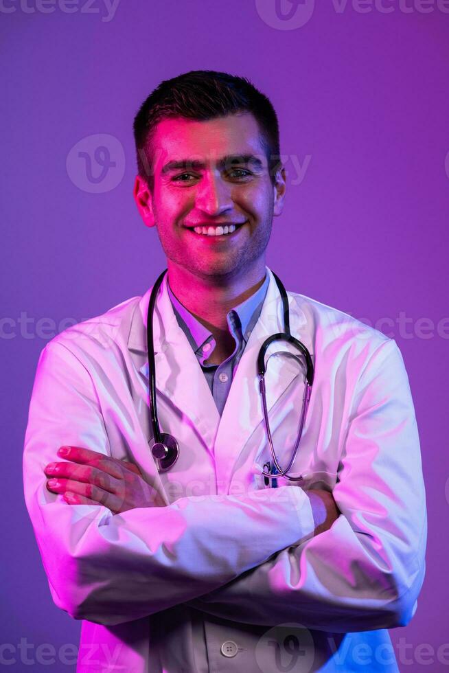 retrato do herói dentro branco casaco. alegre sorridente jovem médico com estetoscópio dentro médico hospital em pé contra azul e Rosa fundo. coronavírus covid-19 Perigo alerta foto