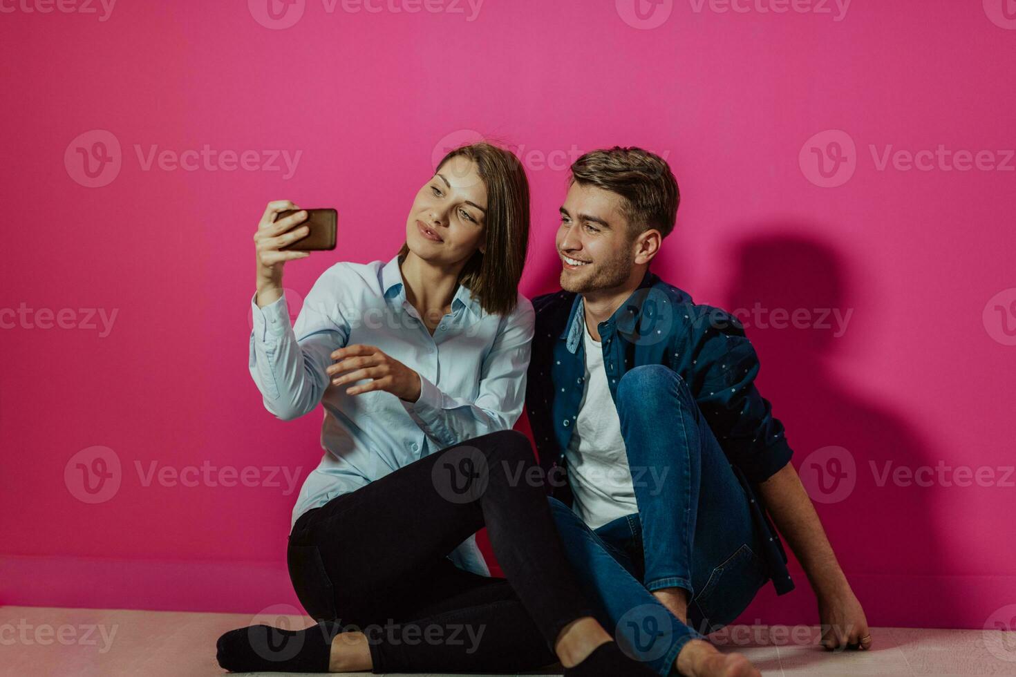 um jovem casal feliz sentado no chão em casa e fazendo selfie foto
