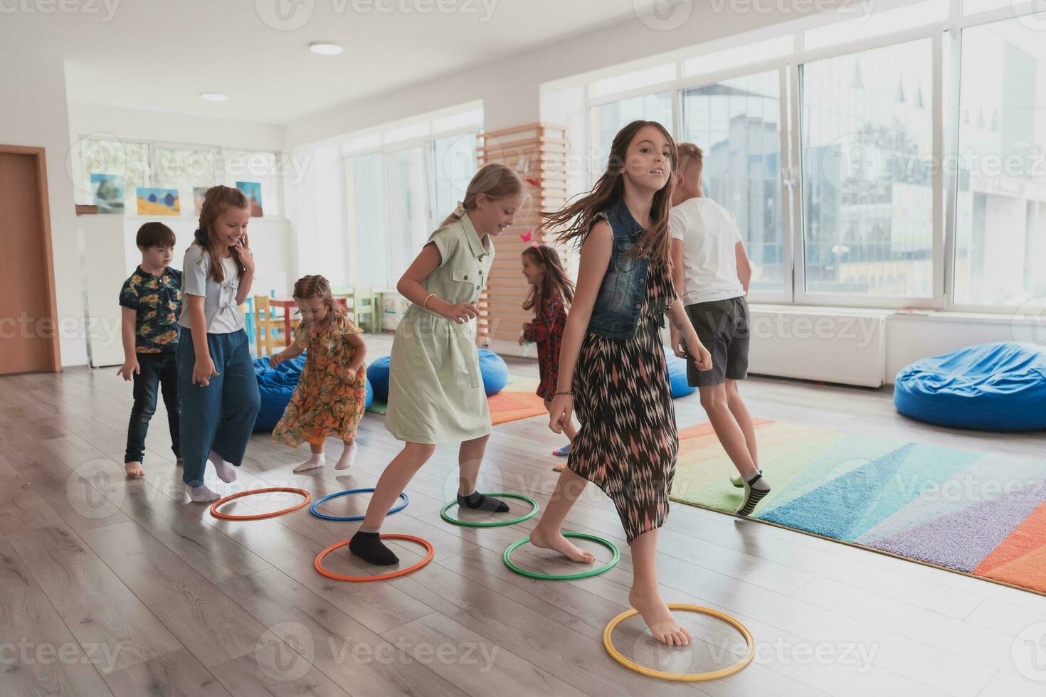 pequeno berçário escola crianças com fêmea professor em chão dentro de casa dentro sala de aula, fazendo exercício. pulando sobre hula aro círculos rastrear em a chão. foto