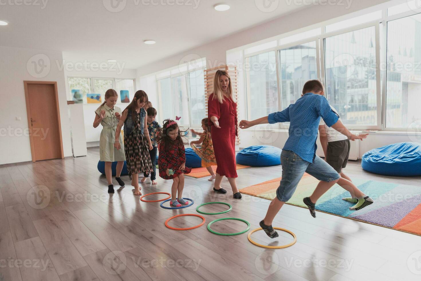 pequeno berçário escola crianças com fêmea professor em chão dentro de casa dentro sala de aula, fazendo exercício. pulando sobre hula aro círculos rastrear em a chão. foto