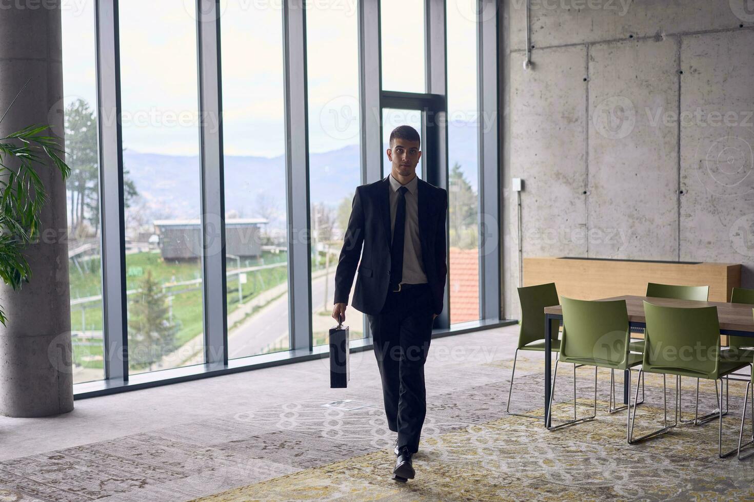 uma confiante homem de negocios com uma pasta passos largos através uma moderno escritório, exalando carisma e determinação, simbolizando sucesso e profissional excelência. foto