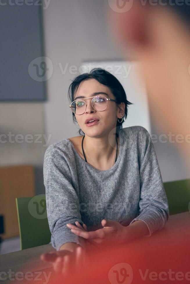 dentro uma moderno escritório, uma jovem sorrir empresária com óculos com confiança explica e apresenta vários o negócio Ideias para dela colegas, exibindo dela profissionalismo e perícia. foto