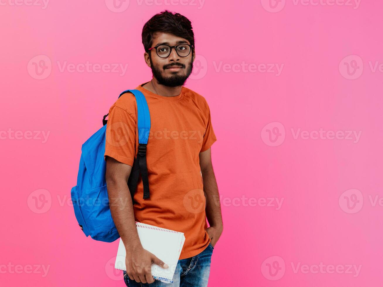 indiano aluna com azul mochila, óculos e caderno posando em Rosa fundo. a conceito do Educação e escolaridade. Tempo para ir costas para escola foto