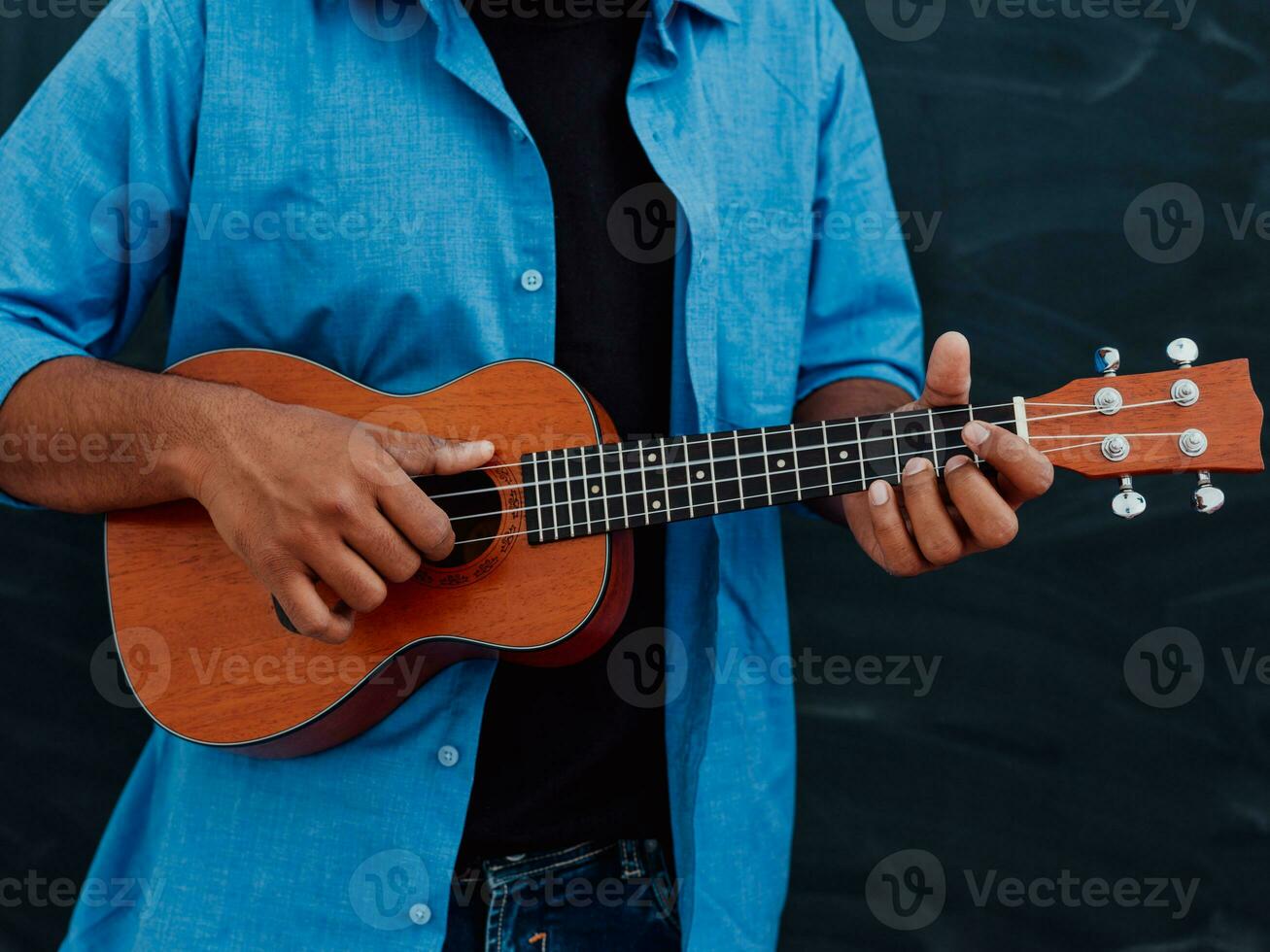 indiano jovem homem dentro uma azul camisa e óculos jogando a guitarra dentro frente do a escola quadro-negro foto