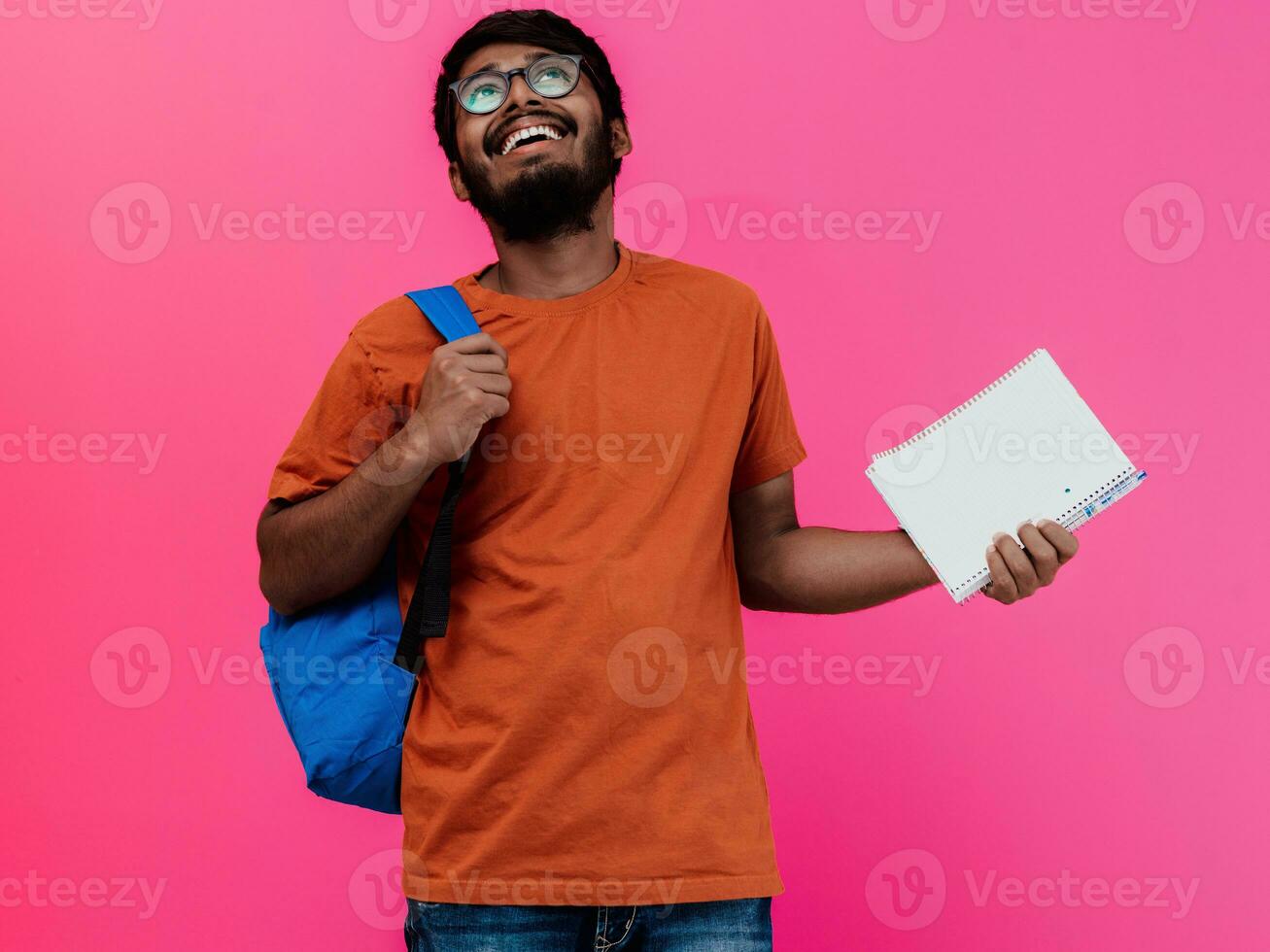 indiano aluna com azul mochila, óculos e caderno posando em Rosa fundo. a conceito do Educação e escolaridade. Tempo para ir costas para escola foto