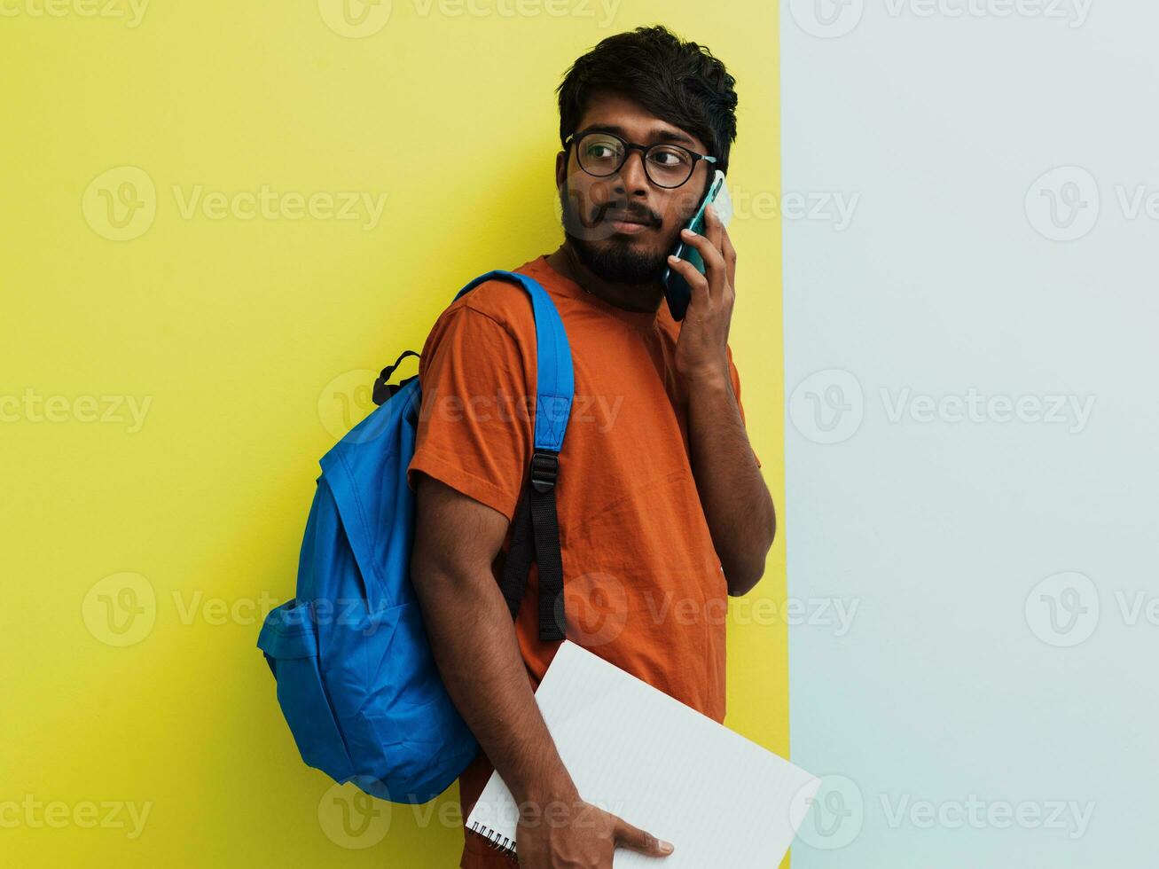 indiano aluna com azul mochila, óculos e caderno usando espertinho e posando em verde Cinza fundo. a conceito do Educação e escolaridade. Tempo para ir costas para escola foto