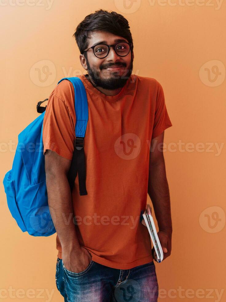 indiano aluna com azul mochila, óculos e caderno posando em laranja fundo. a conceito do Educação e escolaridade. Tempo para ir costas para escola foto