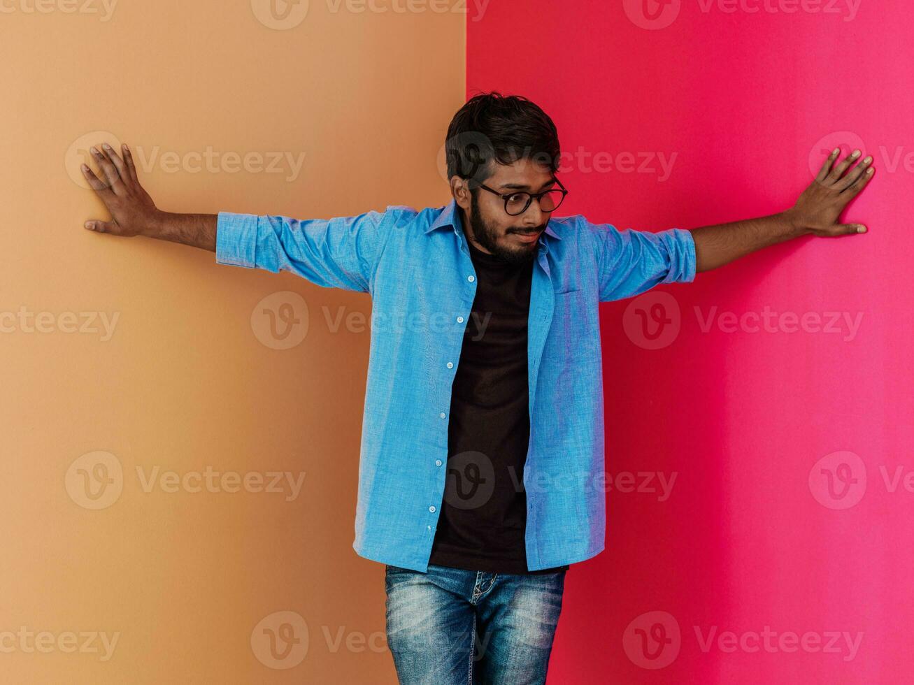 uma jovem indiano aluna dentro uma azul camisa com óculos posando em rosa-laranja fundo foto