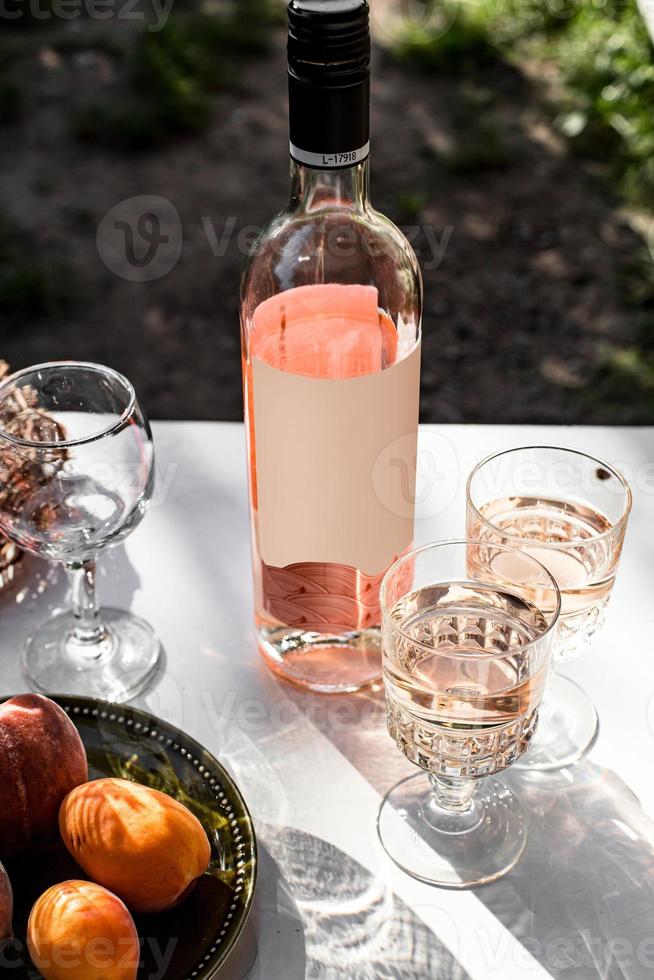 vinho rosado em taças em garrafas douradas com flores e frutas foto