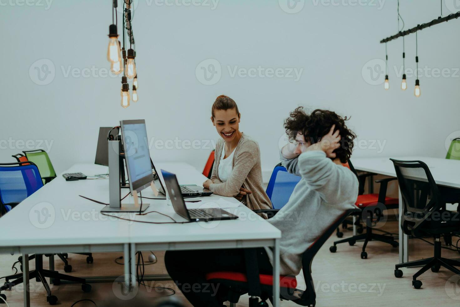 dois colegas trabalhando em uma projeto dentro moderno comece escritórios. cara com afro corte de cabelo e uma fêmea Loiras empregado trabalhando às a escritório. foto