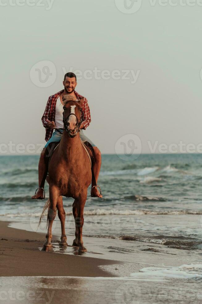 um homem moderno em roupas de verão gosta de andar a cavalo em uma bela praia ao pôr do sol. foco seletivo foto