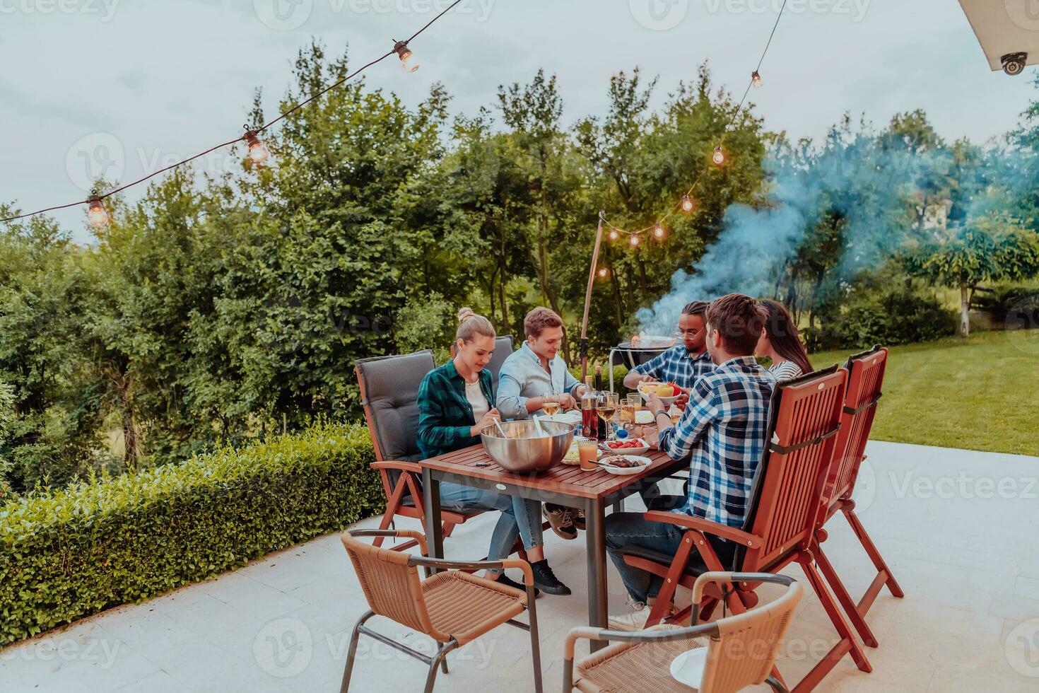 uma grupo do jovem diverso pessoas tendo jantar em a terraço do uma moderno casa dentro a tarde. Diversão para amigos e família. celebração do feriados, casamentos com churrasco. foto