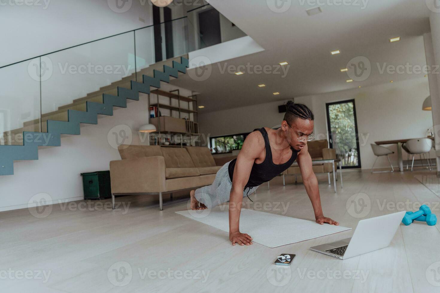 Treinamento às lar. desportivo homem fazendo Treinamento enquanto assistindo conectados tutorial em computador portátil, exercício dentro vivo sala, livre espaço foto