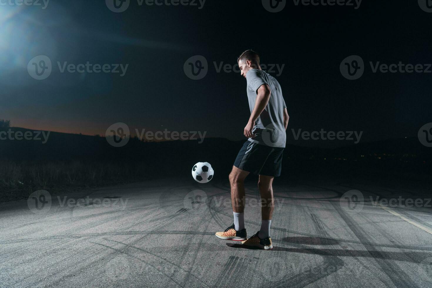 retrato do uma jovem bonito futebol jogador homem em uma rua jogando com uma futebol bola. foto