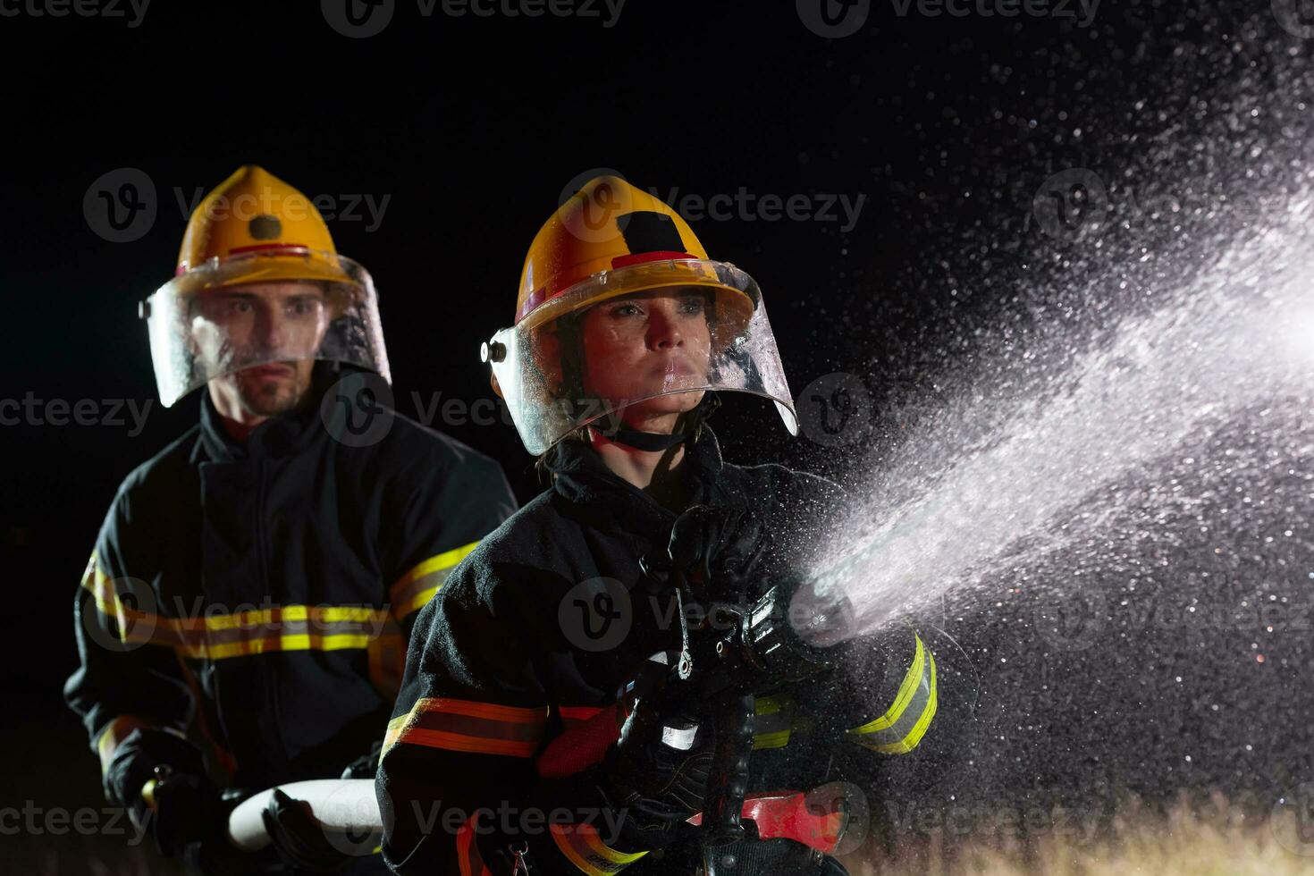 bombeiros usando uma água mangueira para eliminar uma fogo perigo. equipe do fêmea e masculino bombeiros dentro perigoso resgate missão. foto