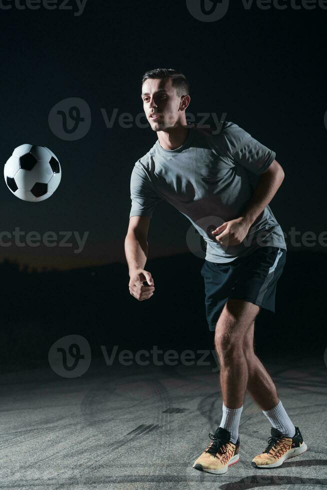 retrato do uma jovem bonito futebol jogador homem em uma rua jogando com uma futebol bola. foto