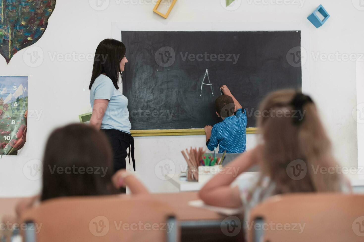 elementar escola. a fêmea professor ajudando a criança aluna enquanto escrevendo a responda em a quadro-negro. foto