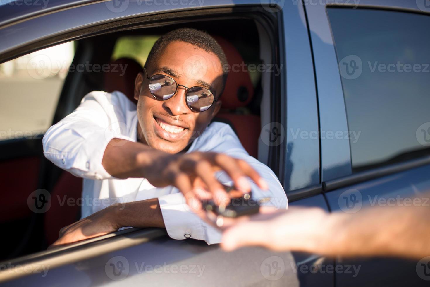 feliz afro-americano em um carro com uma chave, no verão foto