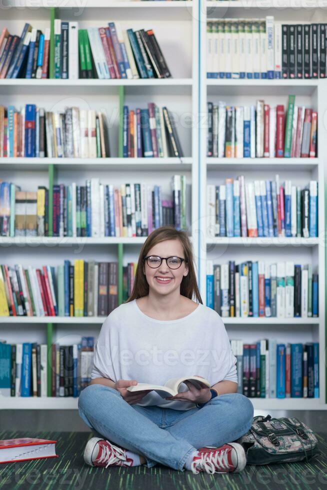 Famale estudante lendo livro na biblioteca foto