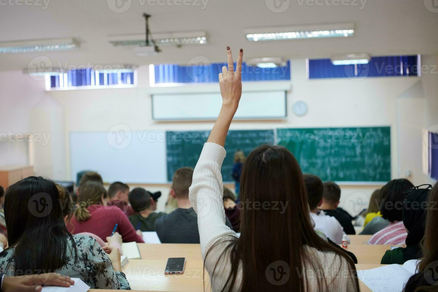 aluna sentada na classe e levantando a mão foto