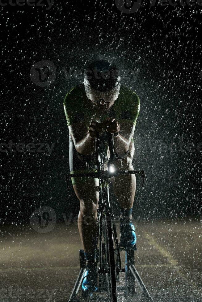 atleta de triatlo andando de bicicleta rápido na noite chuvosa foto