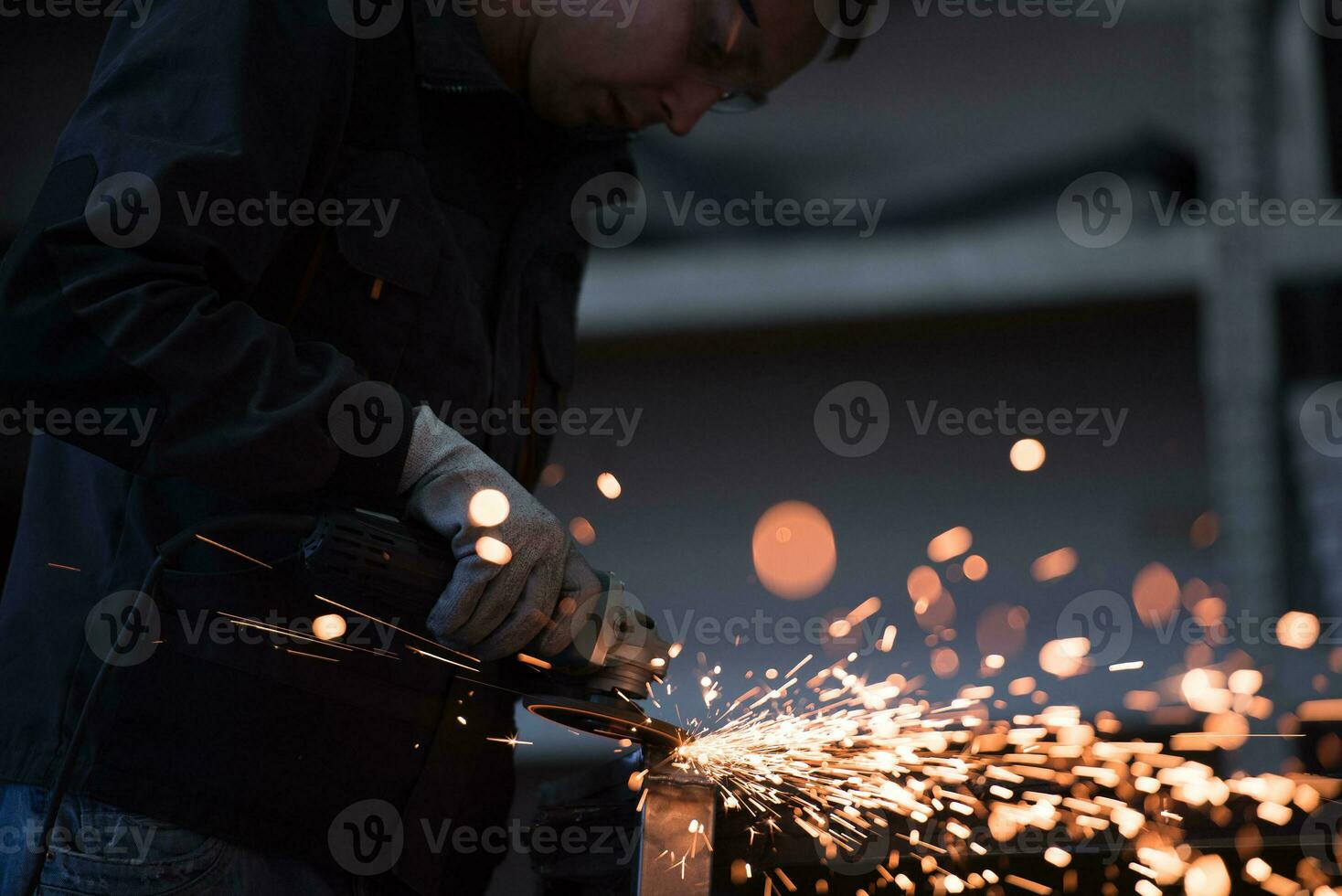 interior da fábrica de engenharia da indústria pesada com trabalhador industrial usando rebarbadora e cortando um tubo de metal. empreiteiro em uniformes de segurança e fabricação de capacetes de estruturas metálicas. foto