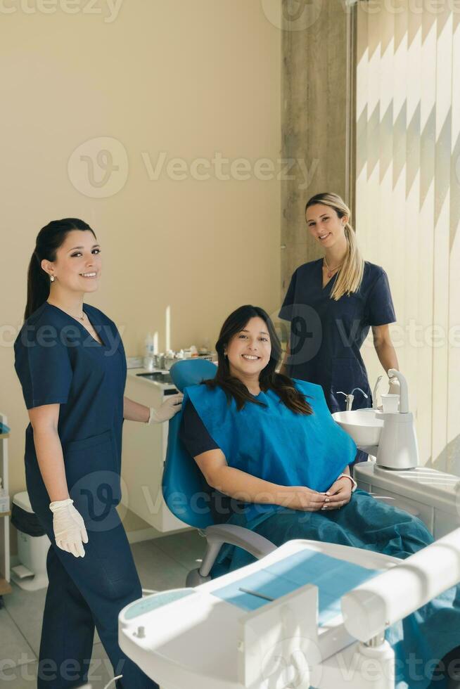 retrato do três mulheres, dentista, assistente e paciente dentro uma dental escritório sorridente e olhando às Câmera. foto