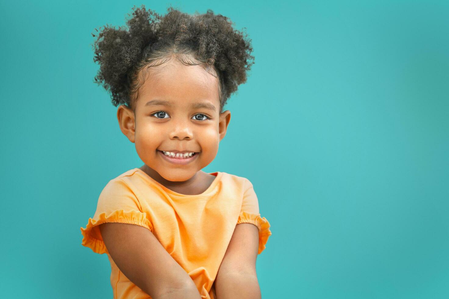 doce pequeno menina ao ar livre com encaracolado cabelo sorridente em azul fundo foto