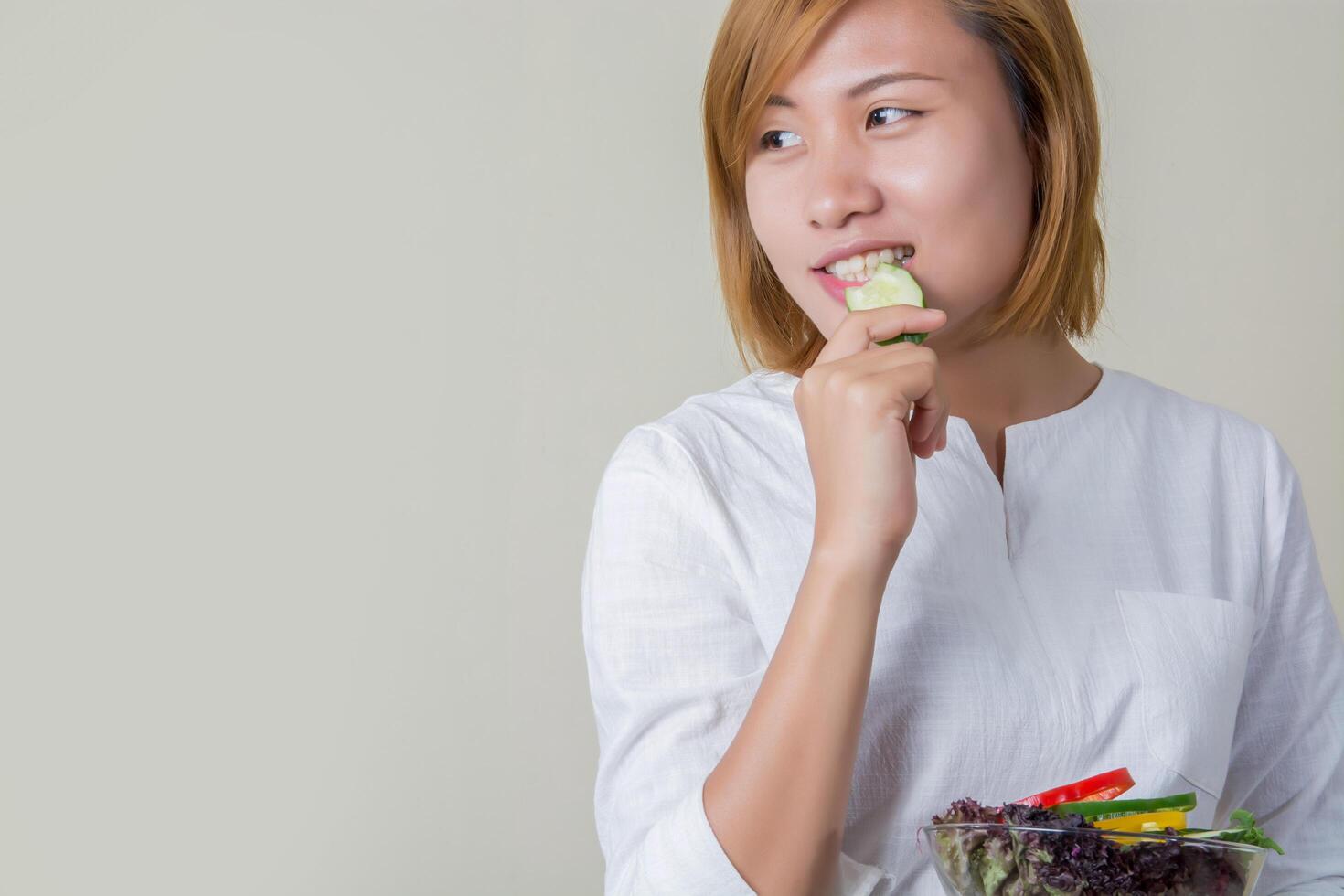 linda mulher em pé segurando uma tigela de salada e comendo alguns vegetais foto