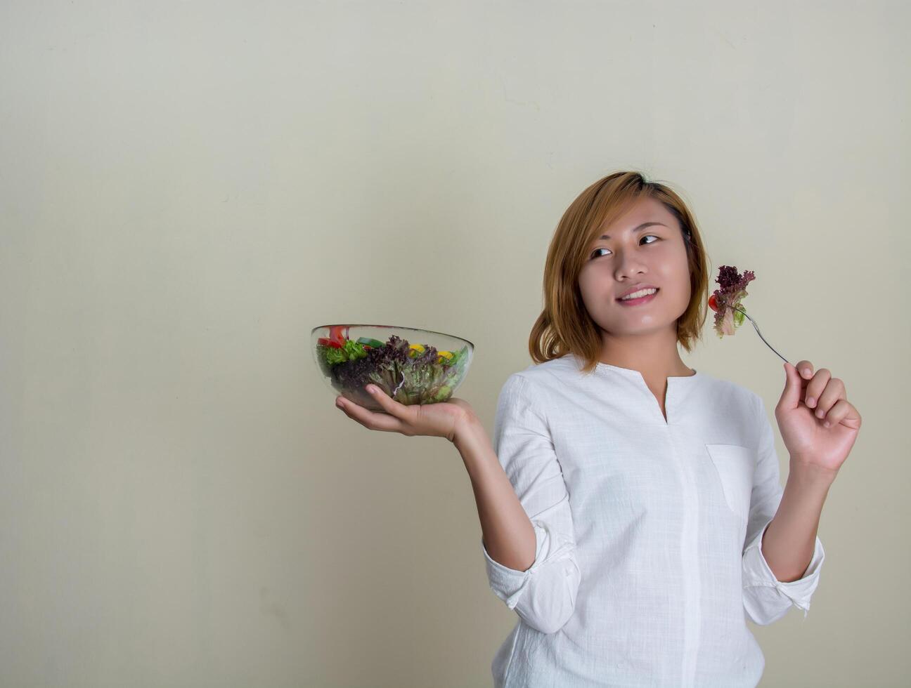 linda mulher em pé segurando uma tigela de salada e comendo alguns vegetais foto