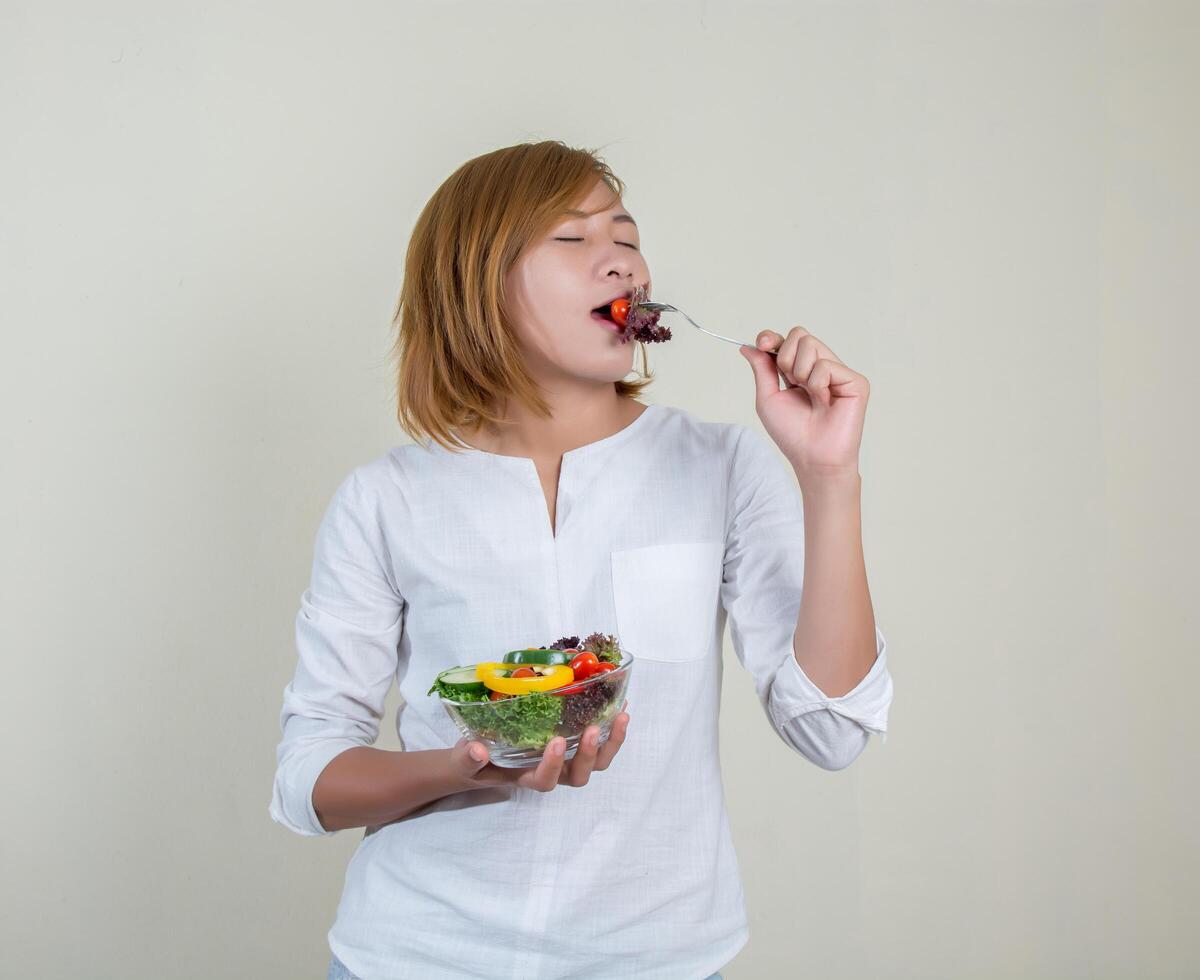 linda mulher em pé segurando uma tigela de salada e comendo alguns vegetais foto