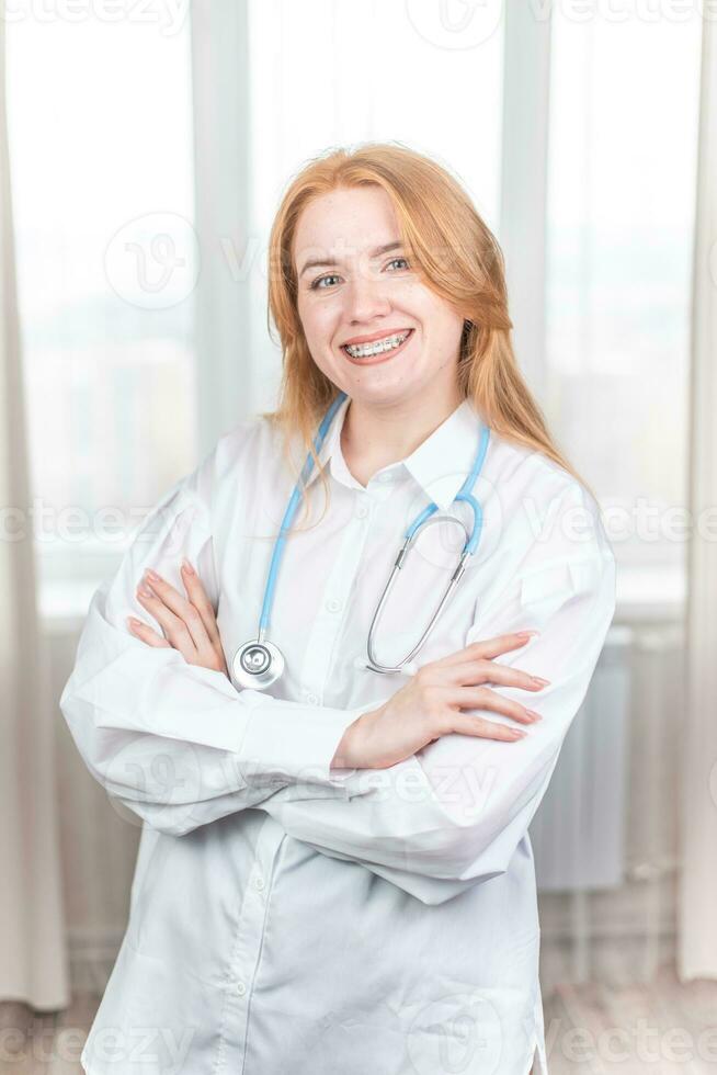 médico conceito. sorridente enfermeira com suspensórios e uma estetoscópio dentro dela mão. feliz e rindo fêmea médico dentro uma branco casaco posando às a Câmera. hospital trabalhador foto