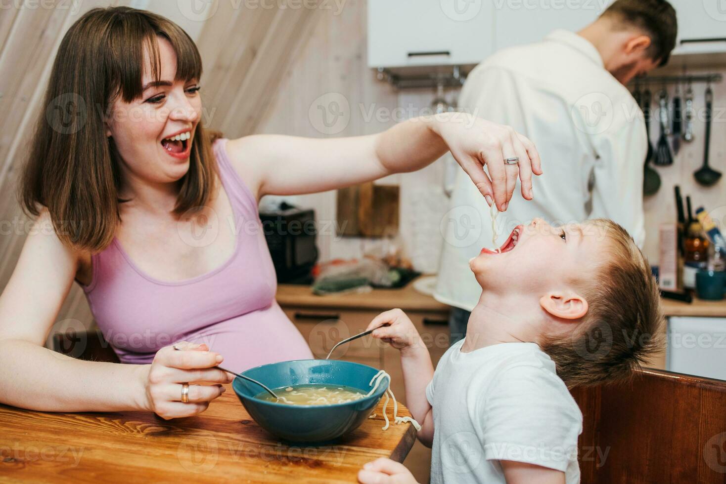 mãe com pai alimentando a criança dentro a cozinha com massa foto