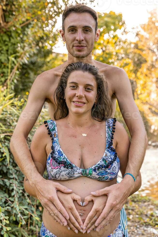 retrato do pais dentro maiôs formando coração placa com mãos em grávida mãe barriga foto