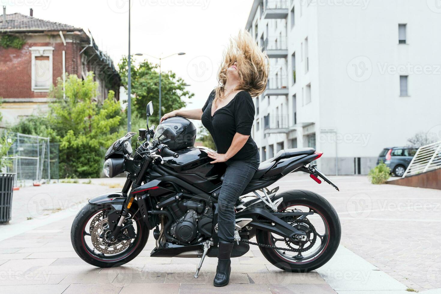 maduro motociclista mulher lança dela loiro cabelo costas equitação a motocicleta foto